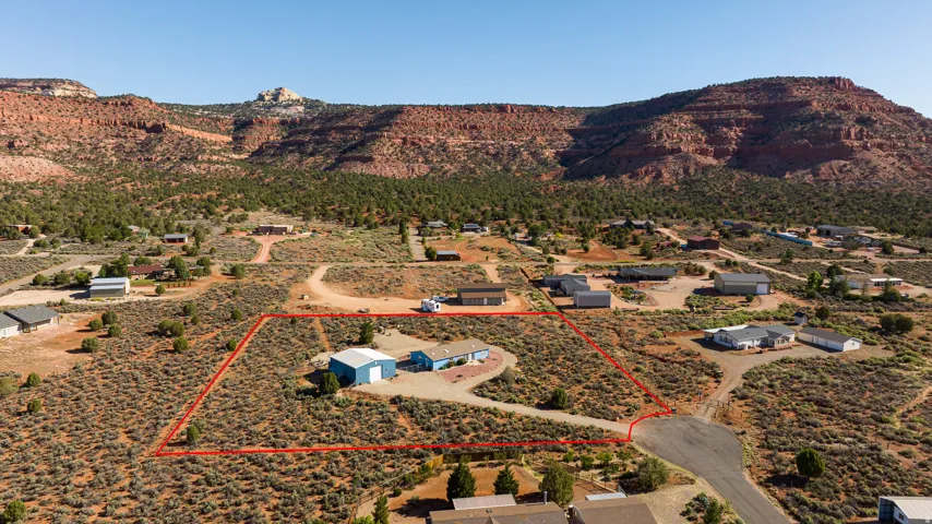 Expansive desert landscape featuring a main residence, a large shop, and a red rock mountain backdrop
