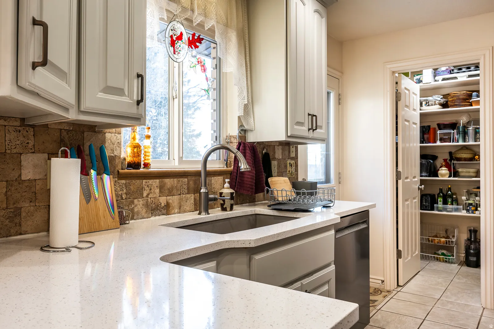 Kitchen featuring light cabinetry, a single-basin sink with a gooseneck faucet, light-toned countertops, and a stone-tile backsplash
