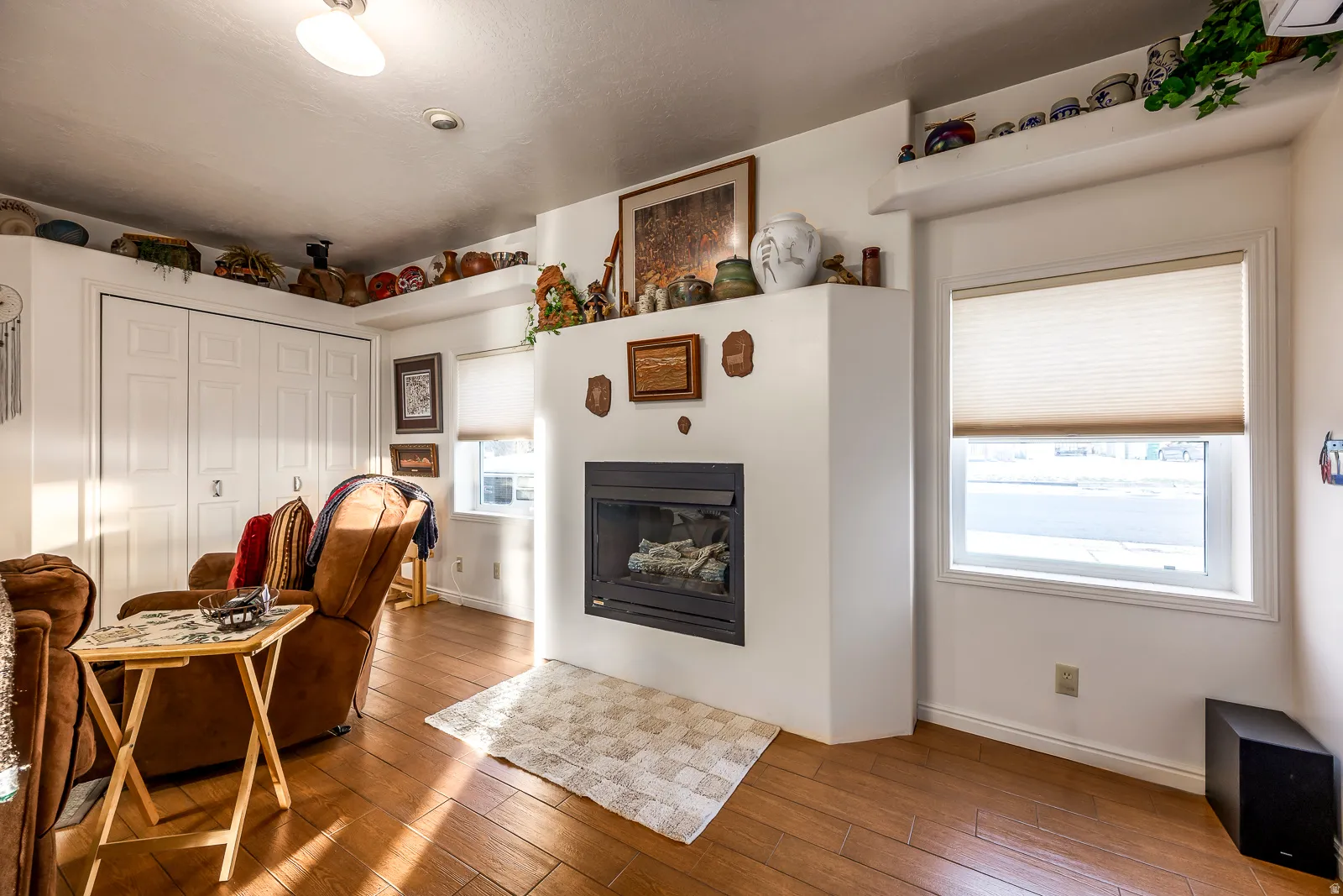 Living area featuring a prominent fireplace with a hearth, wood-finish flooring, recessed lighting, and two windows with blinds