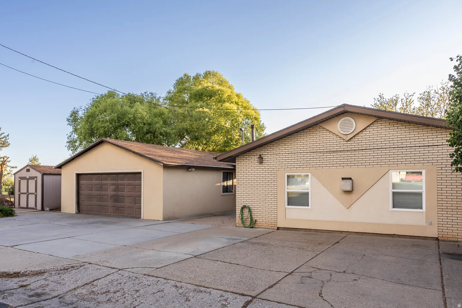 Exterior featuring a two-car garage, an additional detached storage shed, a paved driveway, and light-colored brick siding with stucco accents