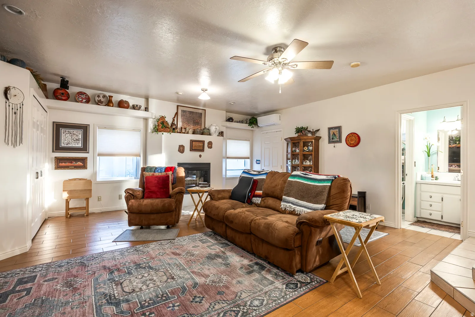 Spacious living area featuring wood-finish flooring, a ceiling fan with integrated lighting, and a prominent fireplace with a mantel