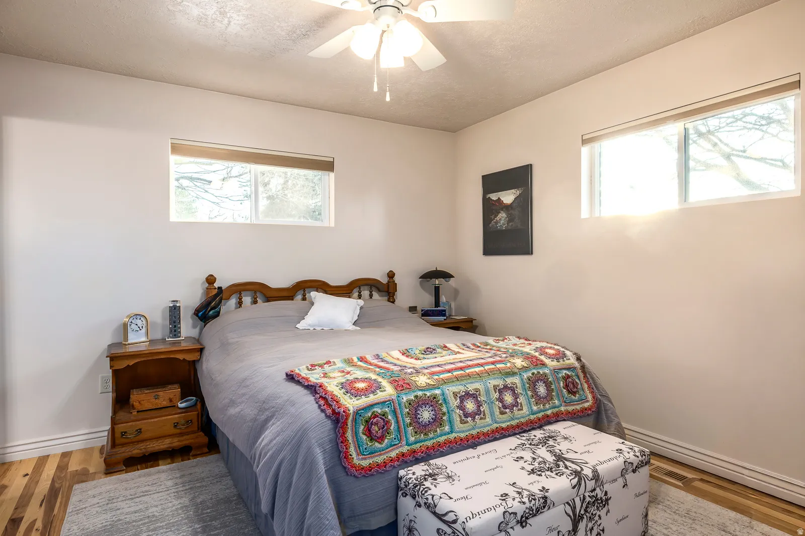 Bright room featuring wood-finish flooring, two windows with roller shades, and a ceiling fan with integrated lighting