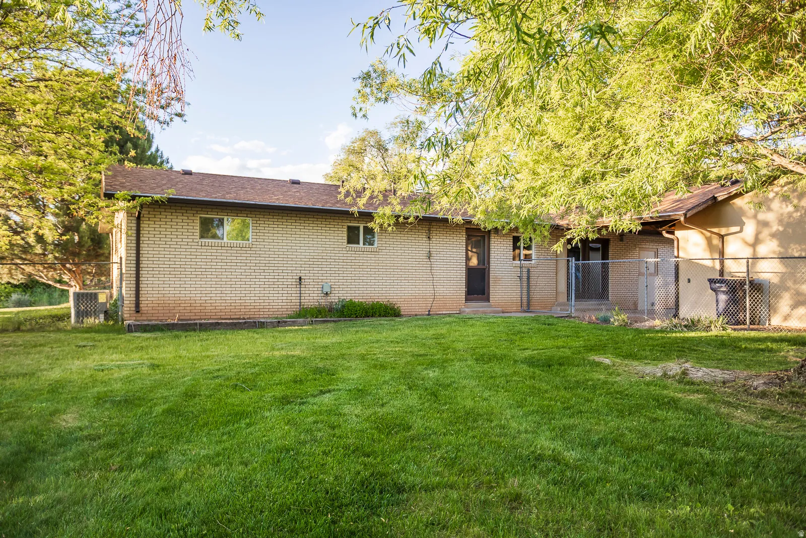 Expansive green lawn with mature trees and a chain-link fence