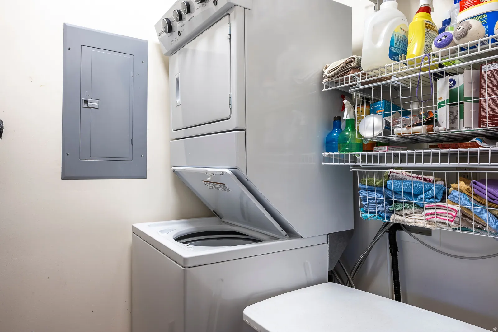Dedicated laundry area featuring a white stacked washer and dryer unit, an electrical service panel, and white wire shelving for storage