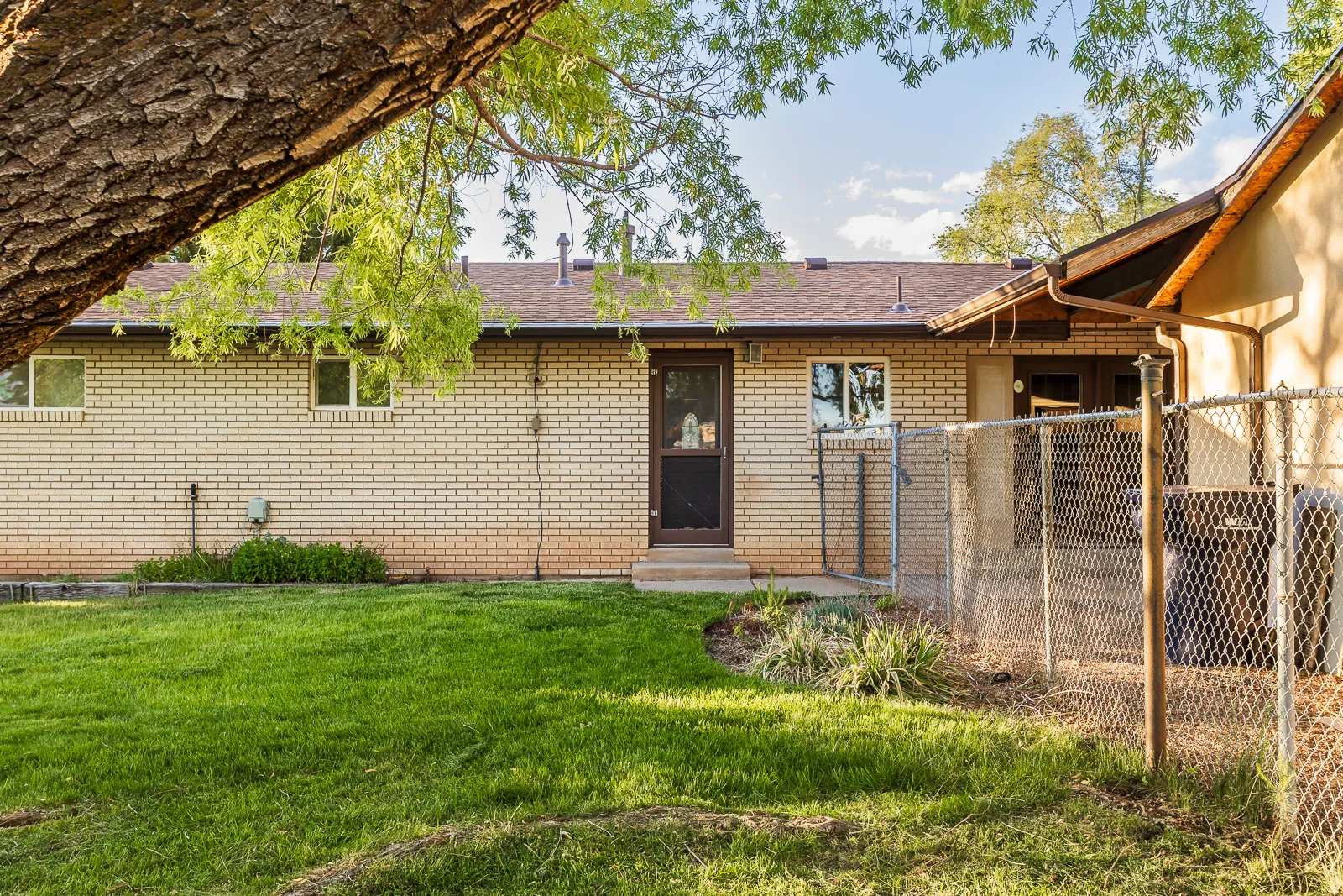 Expansive green lawn with a perimeter chain-link fence, a paved patio area, and mature trees