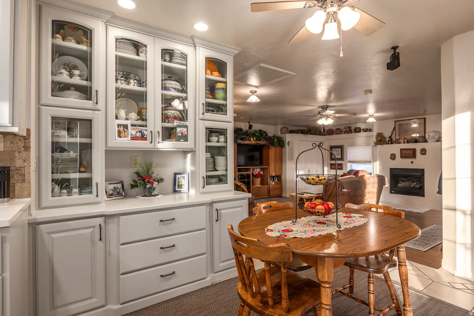 Built-in cabinetry with glass-front uppers and solid lower doors, recessed lighting, a ceiling fan, and a fireplace with a mantel