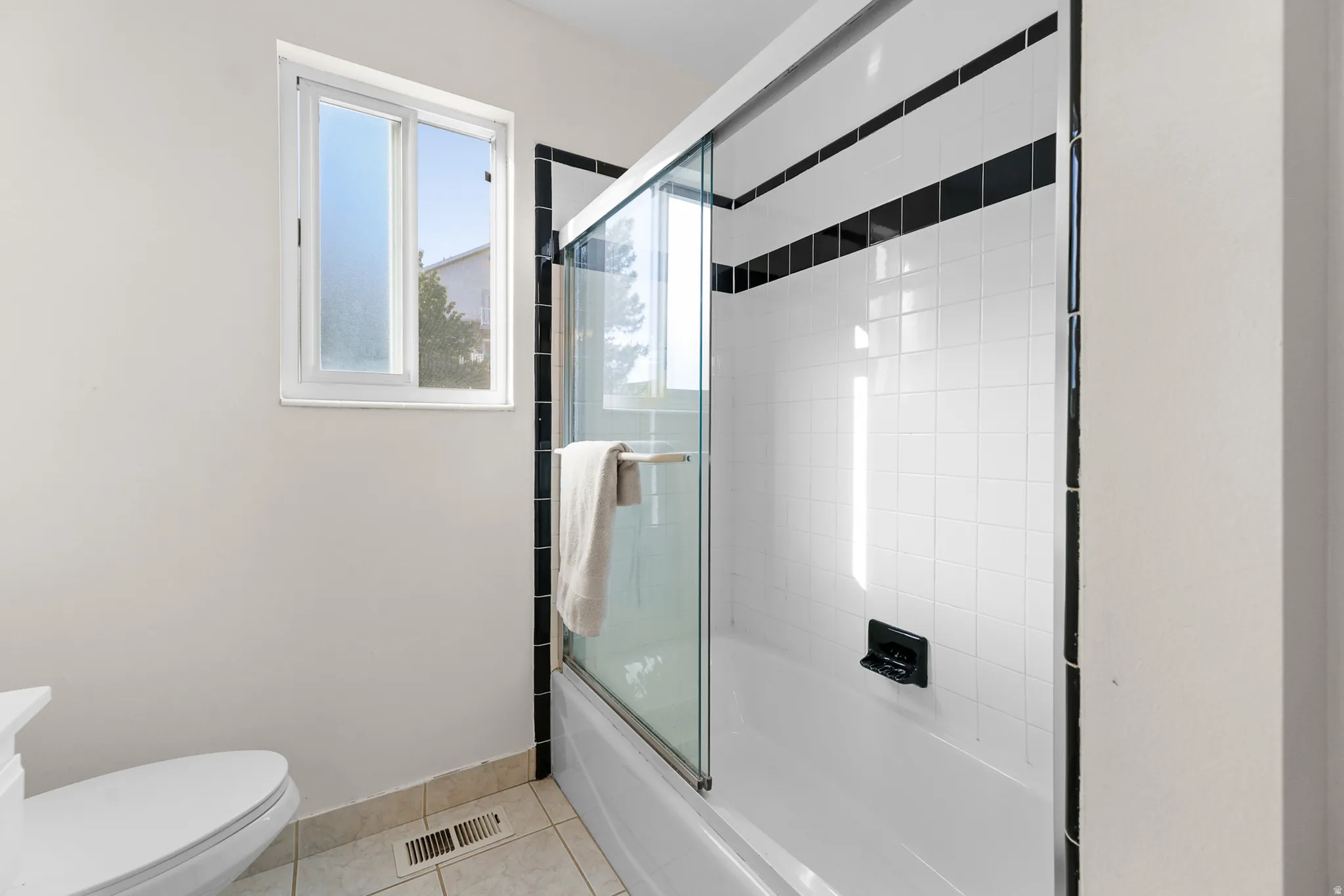Bathtub with clear glass sliding door, white subway tile surround with black accent bands, and a modern dark-finish faucet