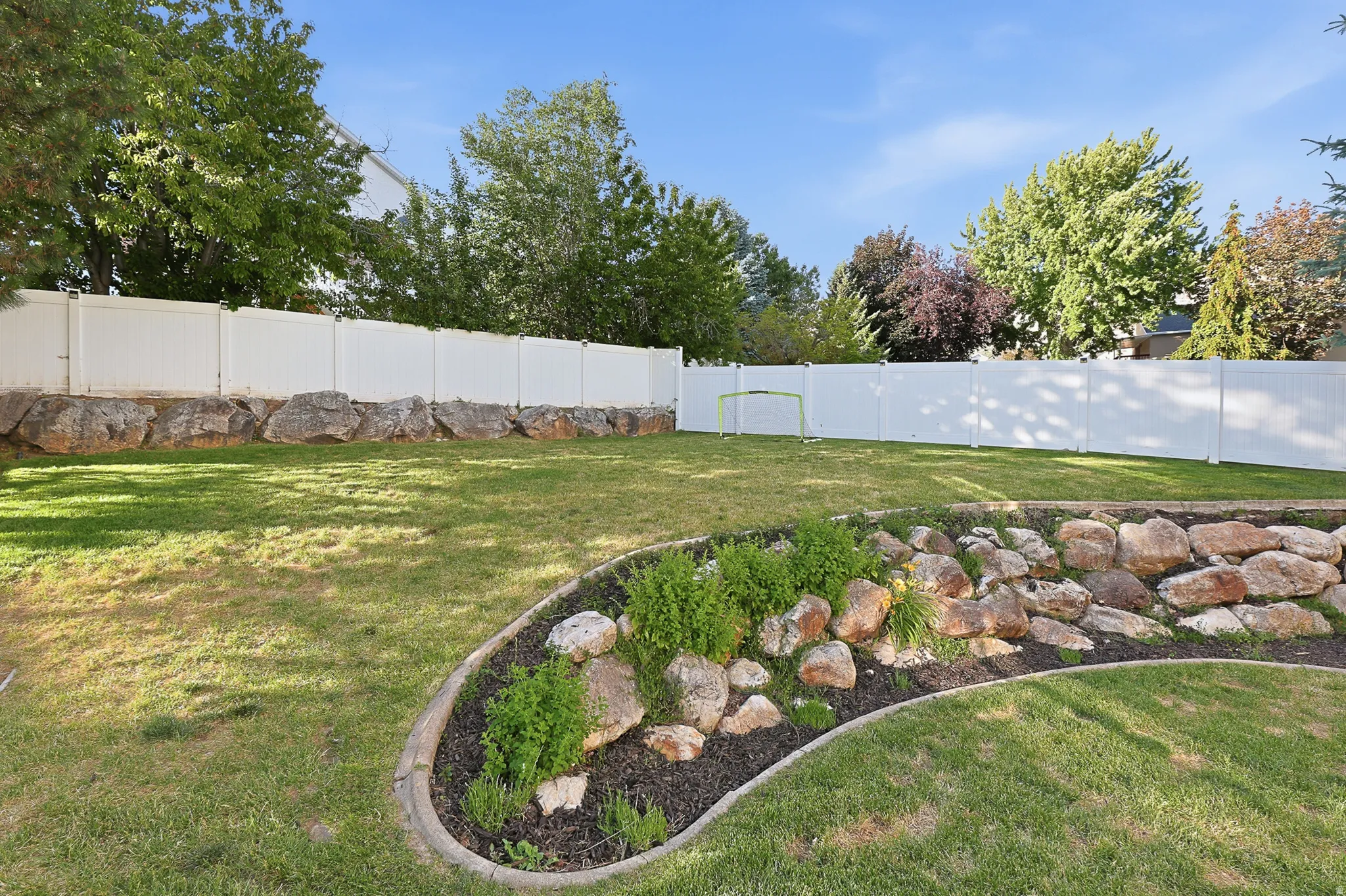 Expansive backyard featuring a manicured lawn, a white privacy fence, and a rock-lined garden bed with plantings