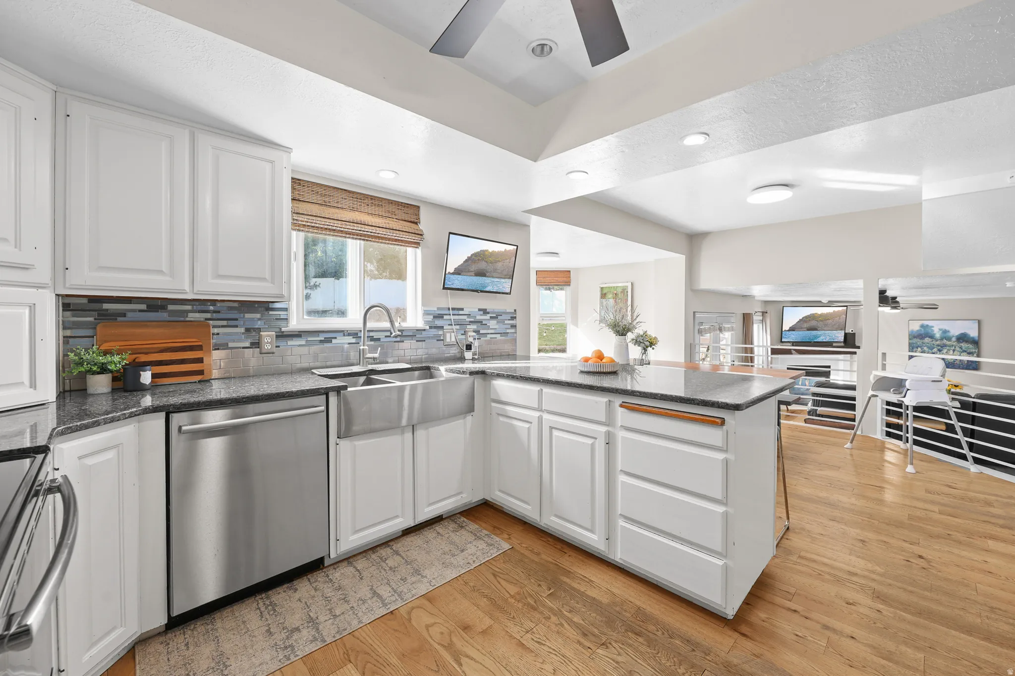 Bright kitchen featuring white cabinetry, granite-style countertops, stainless steel appliances, a farmhouse sink with a gooseneck faucet, and wood-finish flooring
