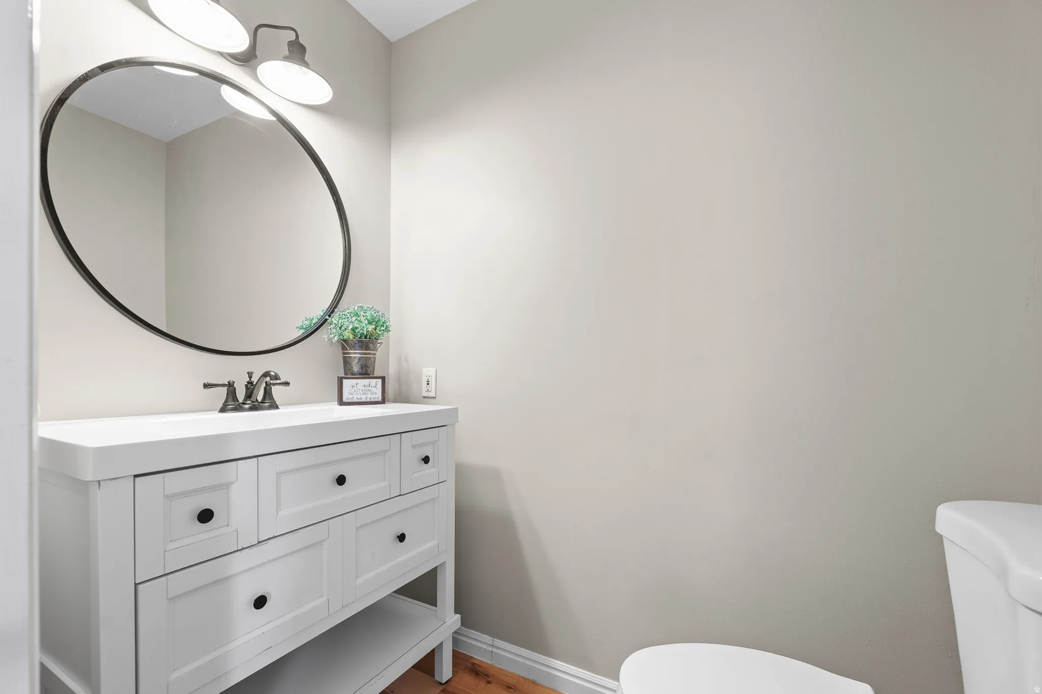 White vanity with black hardware, complementing a circular black-framed mirror and a three-light fixture