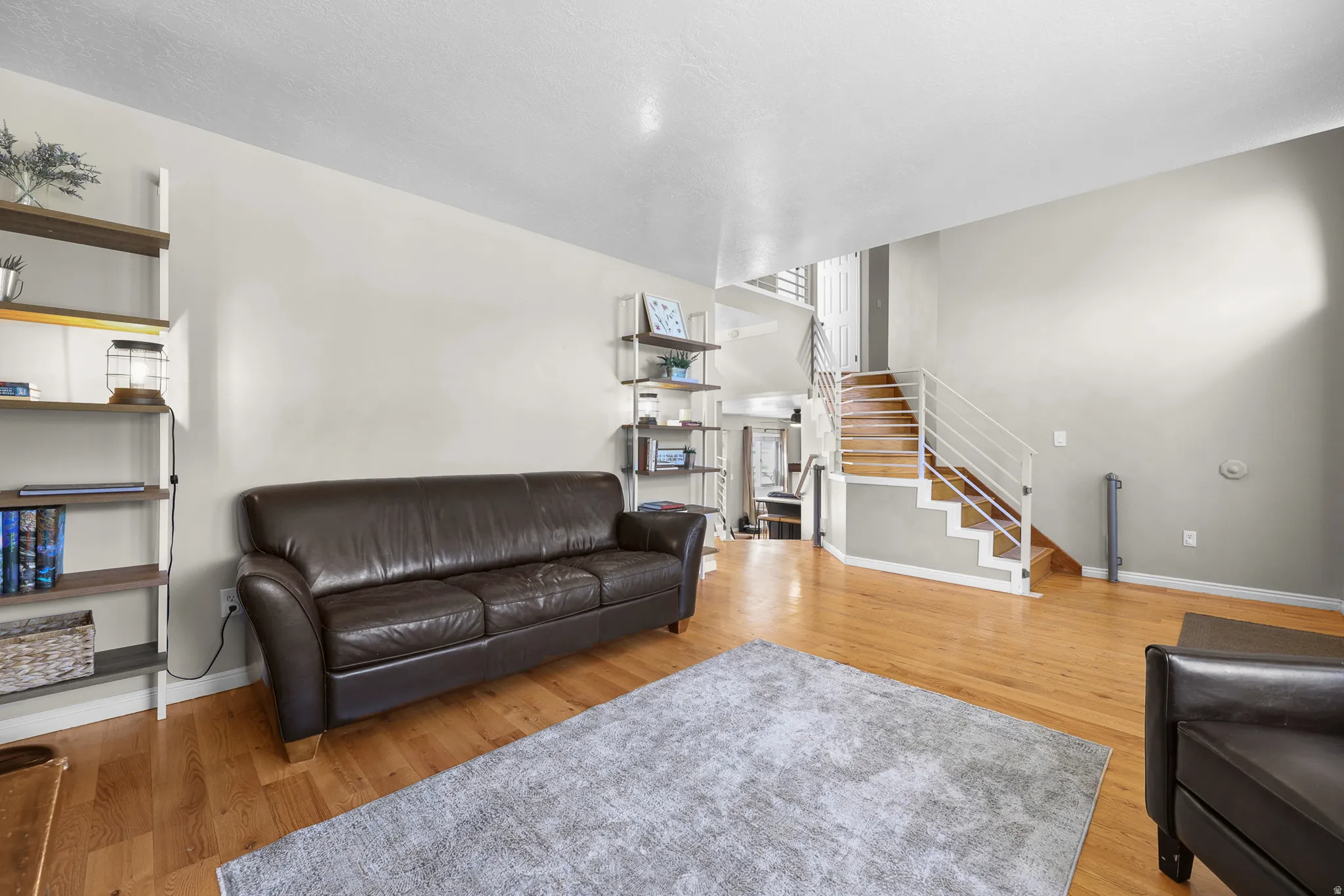 Open-concept living space featuring wood-finish flooring and a contemporary staircase with white metal railings