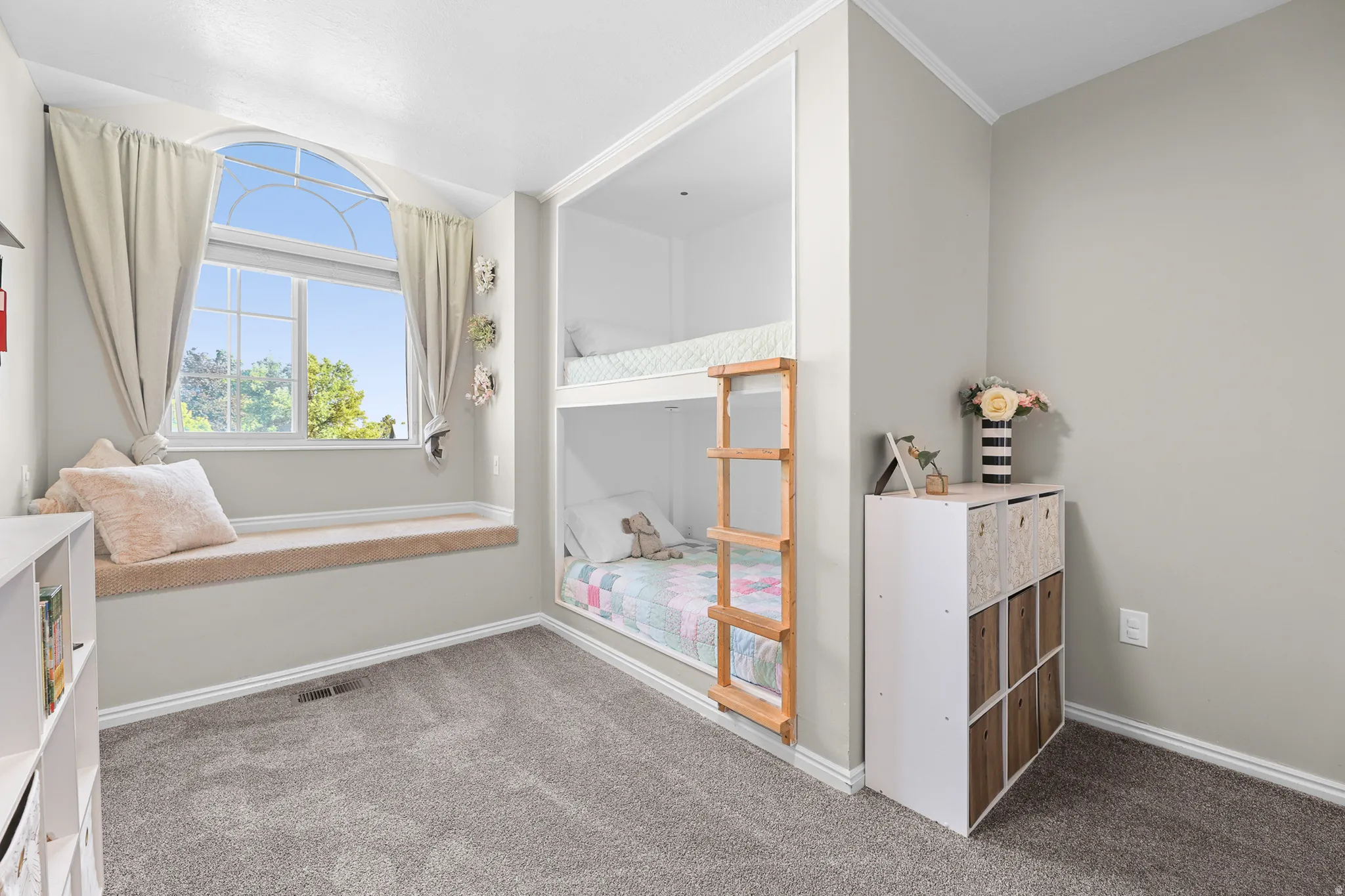 Built-in bunk beds with a wooden ladder, arched window, and a window seat with a cushioned top