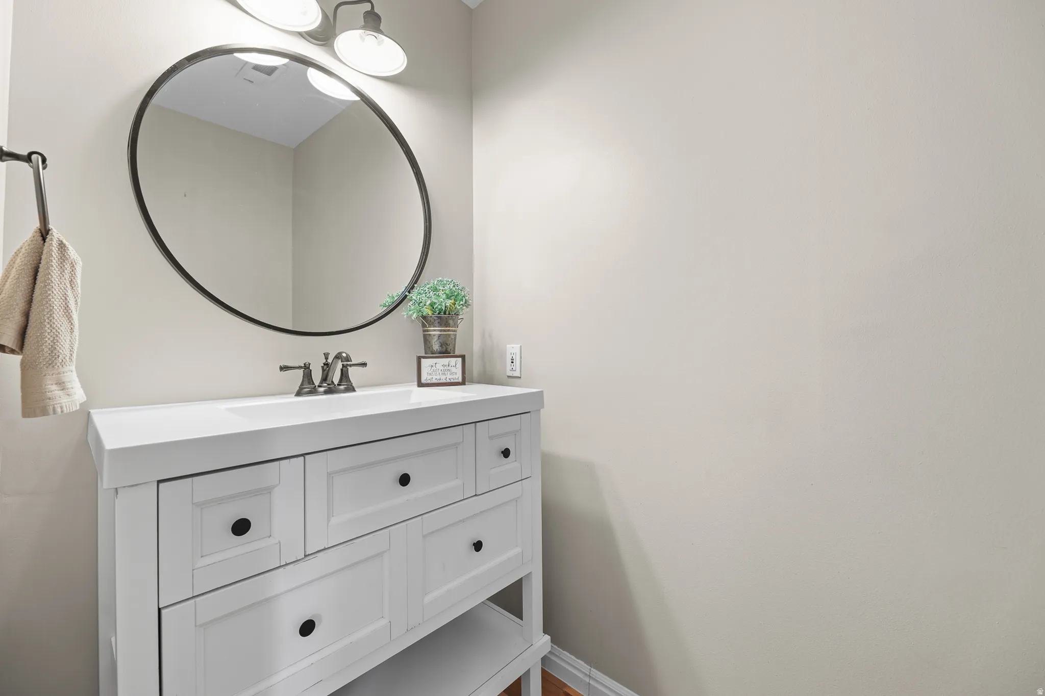 White vanity with integrated sink, black hardware, wall-mounted oval mirror with a black frame, and a two-light vanity fixture