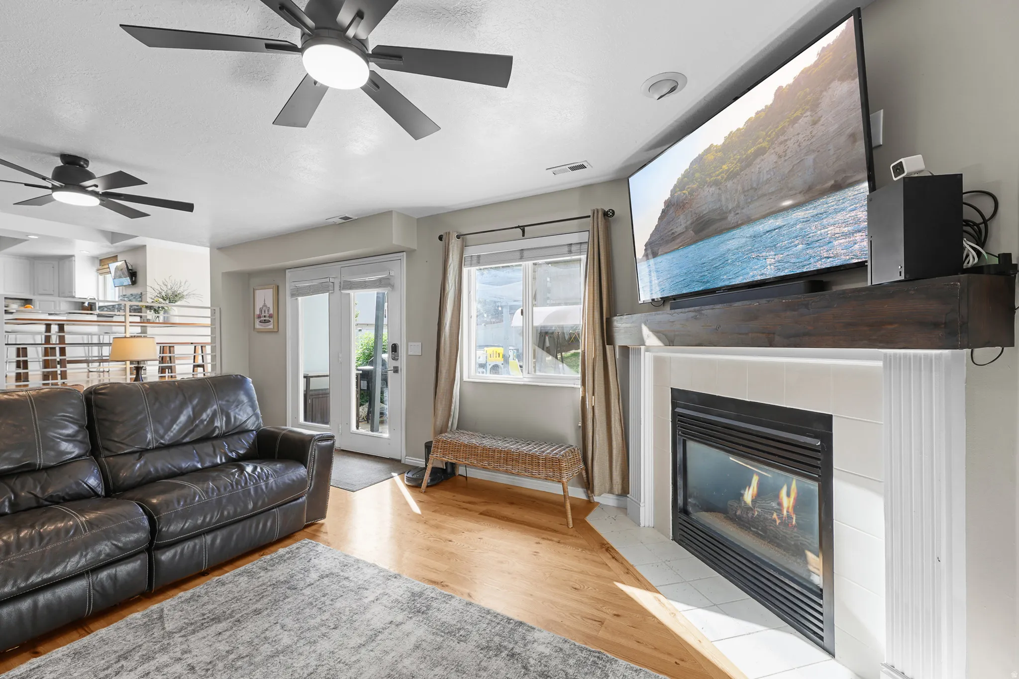 Living area featuring a fireplace with a wood-finish mantel, wood-finish flooring, and multiple ceiling fans