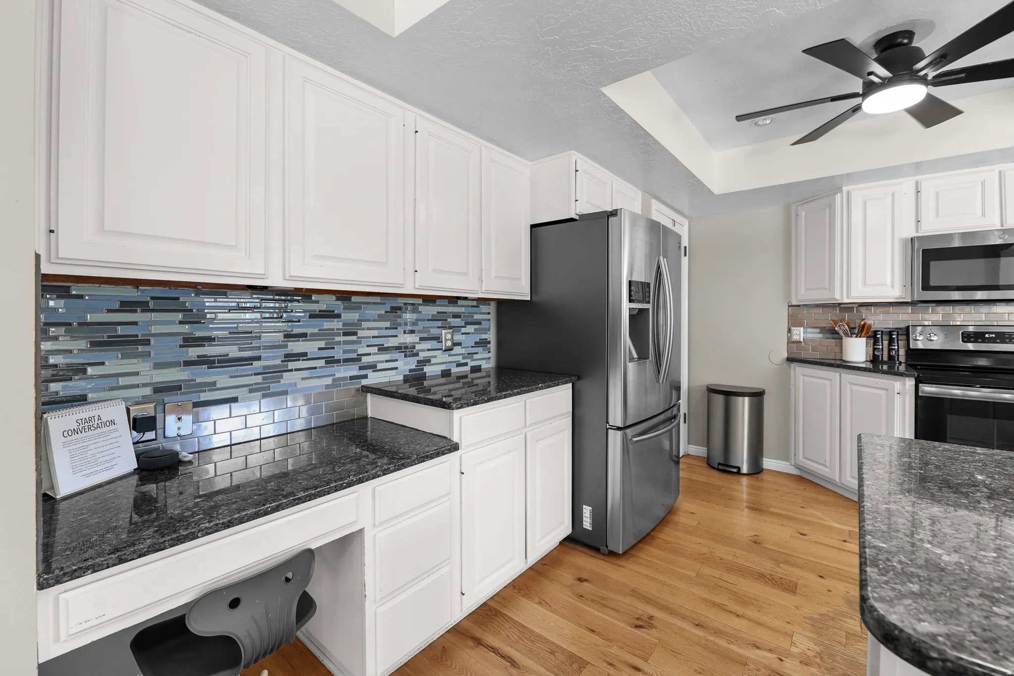 Bright kitchen featuring white cabinetry, dark granite-finish countertops, and wood-finish flooring