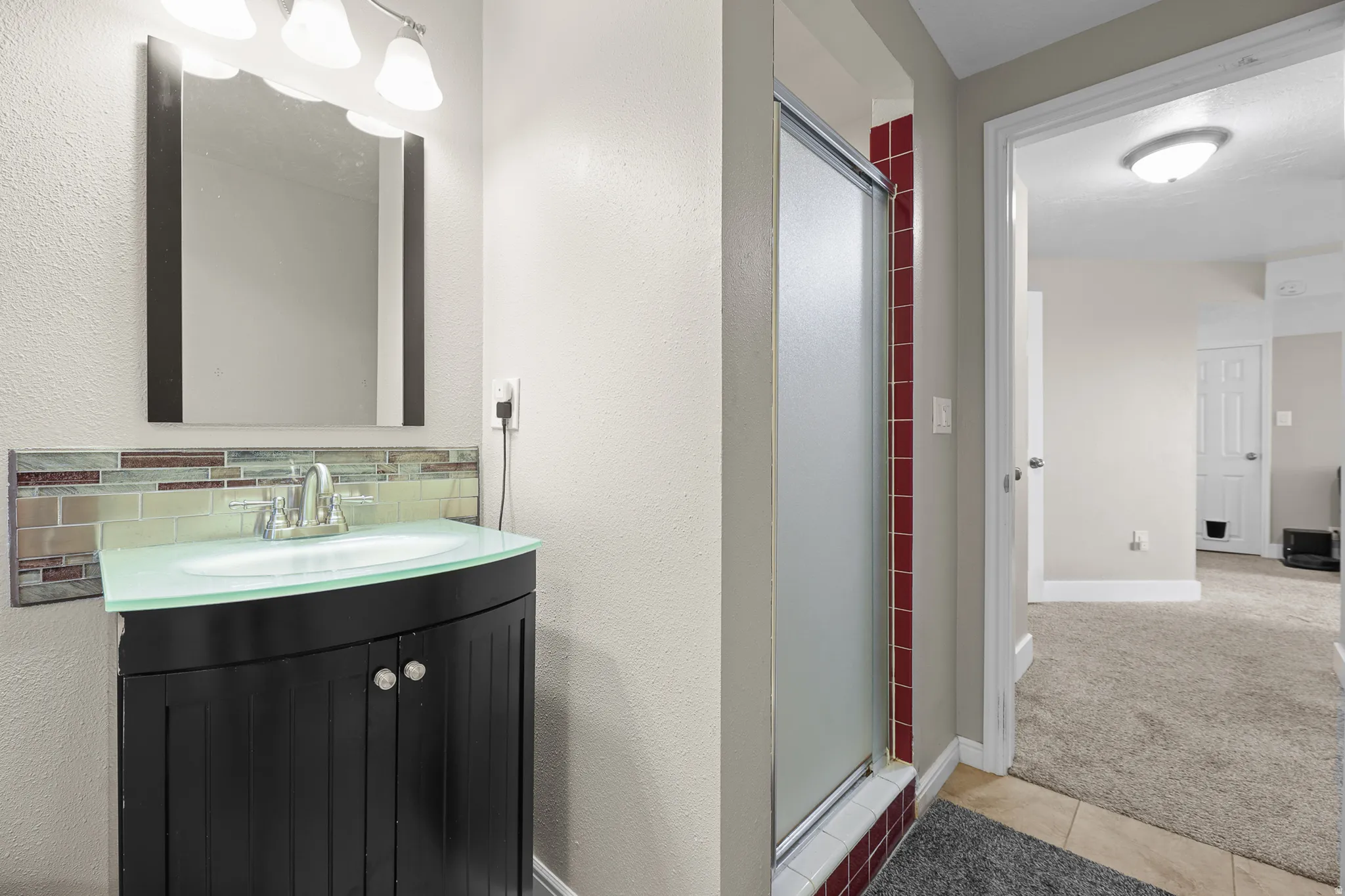Bathroom featuring a dark wood-finish vanity with a curved translucent countertop, a decorative tile backsplash, and a modern rectangular mirror