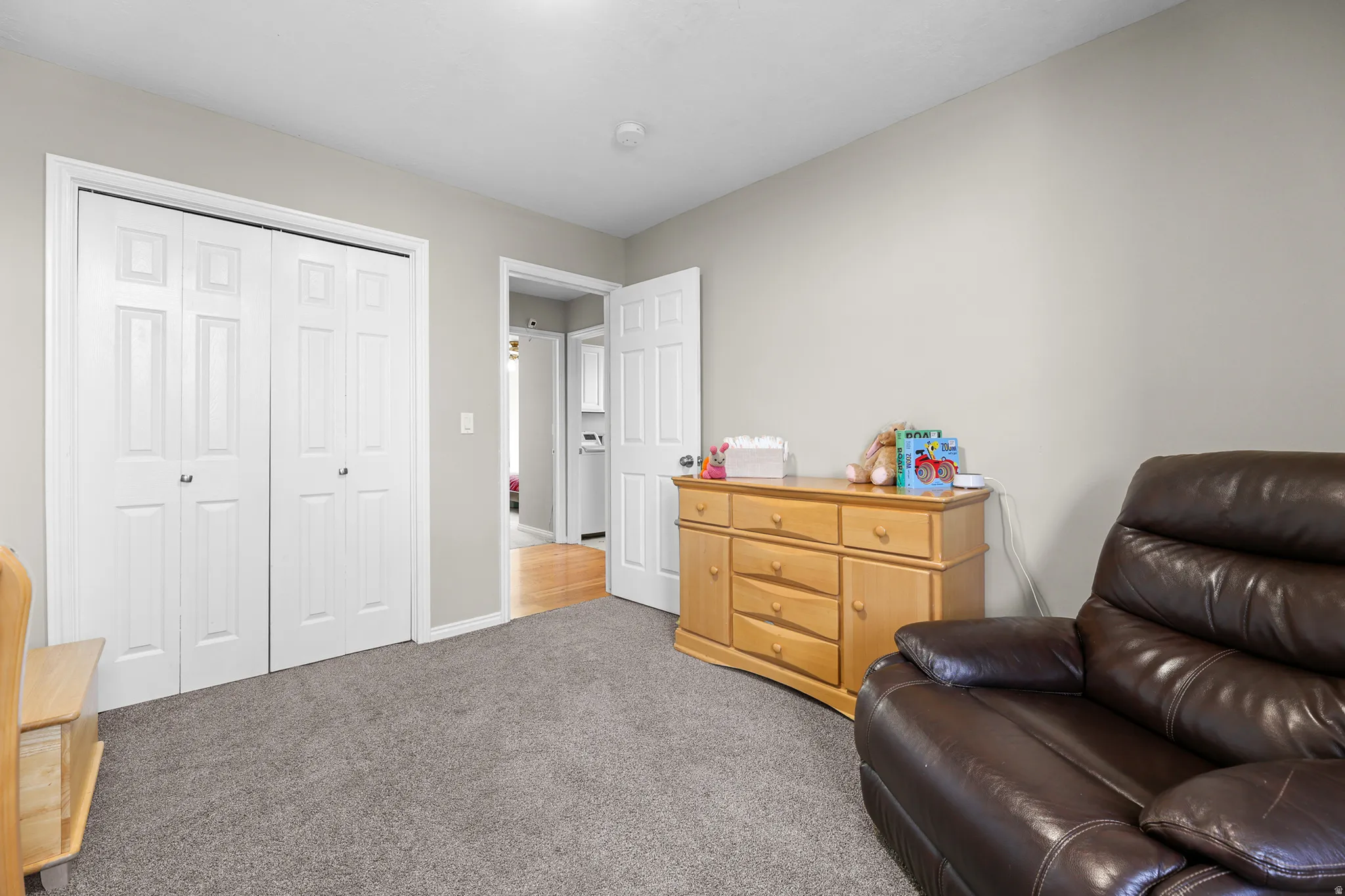 Interior room featuring neutral wall paint, gray carpeting, a built-in closet with bi-fold doors, and a doorway opening to another interior space with wood-finish flooring