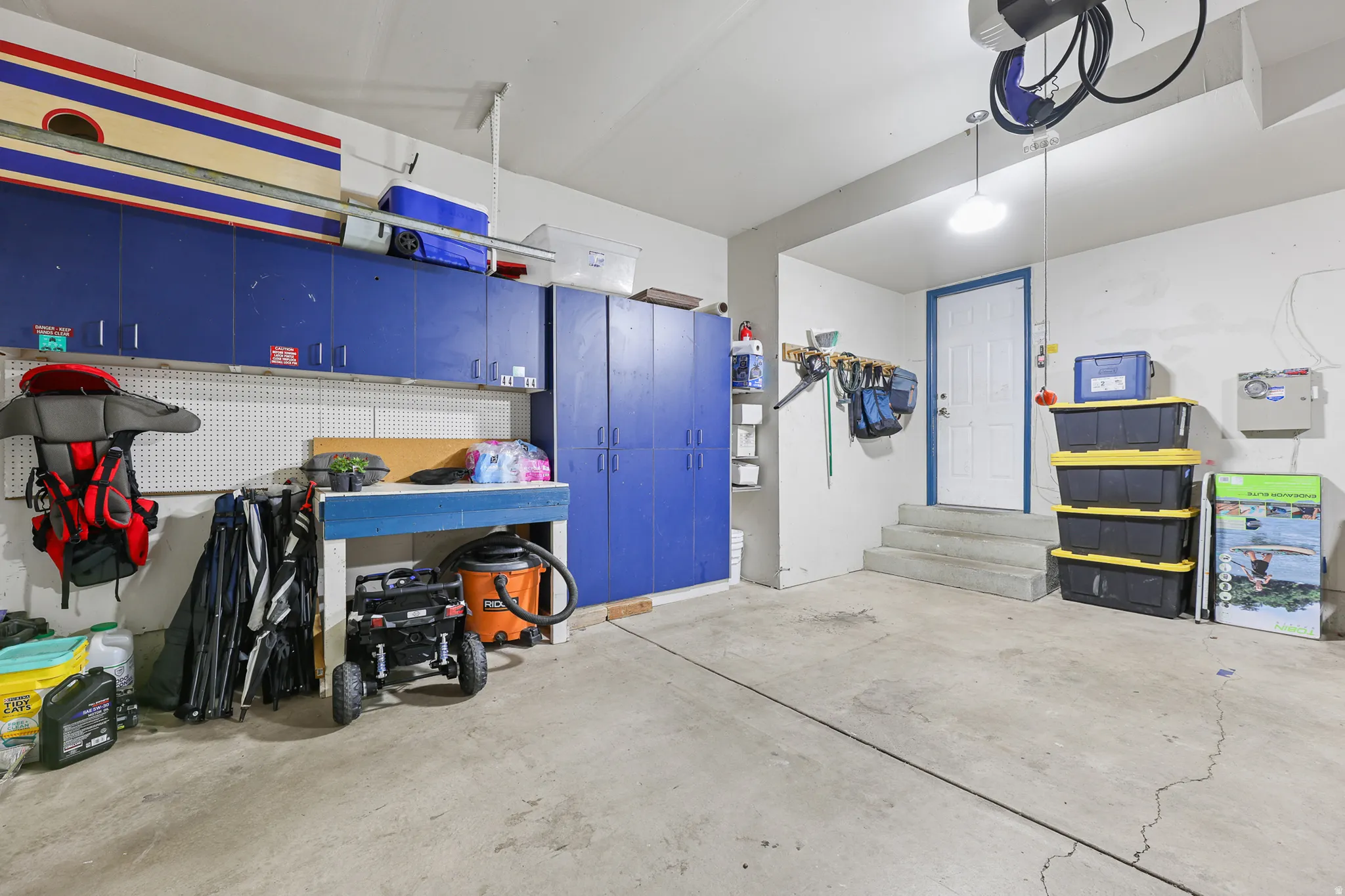 Attached garage featuring concrete flooring, built-in blue cabinetry, white pegboard wall, and a rear access door with steps