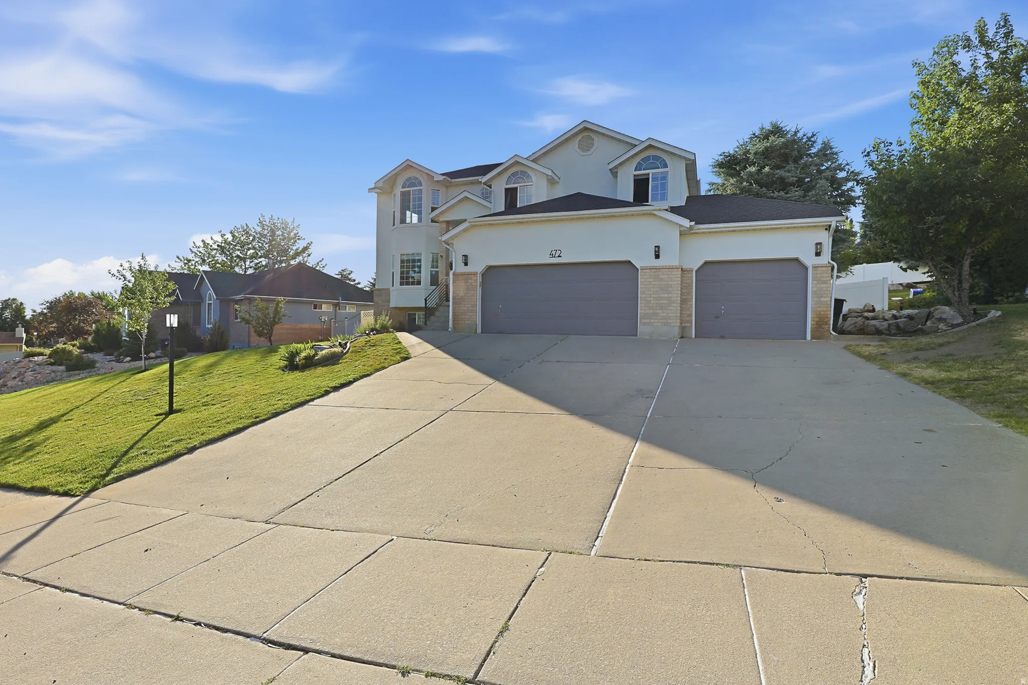 Contemporary residence featuring a two-car garage, concrete driveway, stone accents, arched windows, and a landscaped front yard