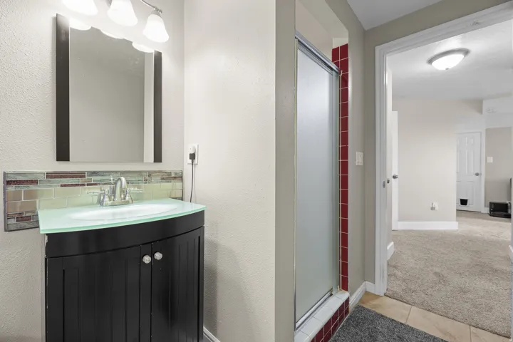 Bathroom featuring a dark wood-finish vanity with a curved translucent countertop, a decorative tile backsplash, and a modern rectangular mirror
