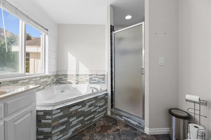 Bathroom featuring a corner jetted tub with tile surround, a separate glass-enclosed shower, a vanity with a countertop, and large format floor tiling