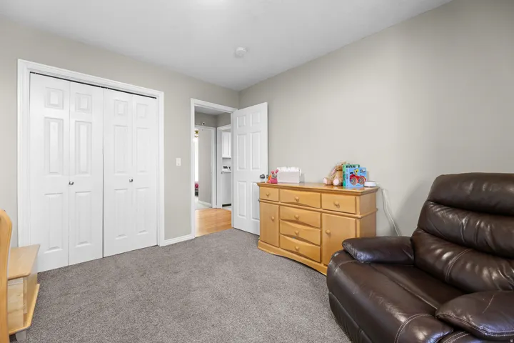 Interior room featuring neutral wall paint, gray carpeting, a built-in closet with bi-fold doors, and a doorway opening to another interior space with wood-finish flooring