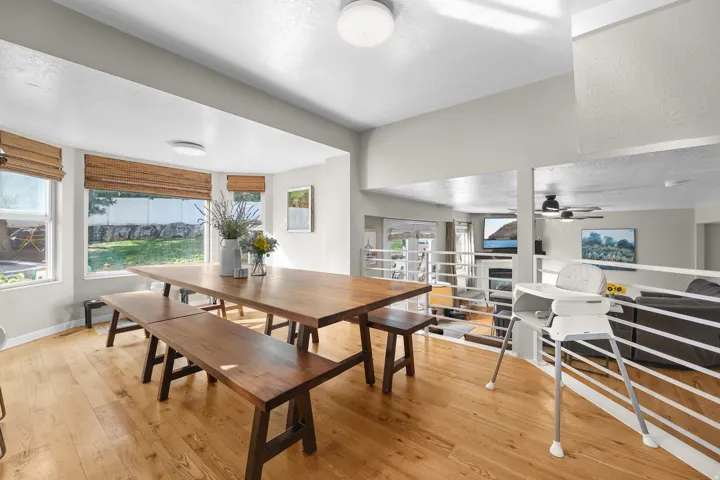 Spacious dining area featuring wood-finish flooring, ample natural light from multiple windows, and a semi-open design overlooking a lower-level living space