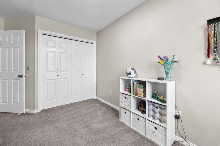 Neutral wall paint and grey carpeting define this room, featuring a white paneled door and double bifold closet doors