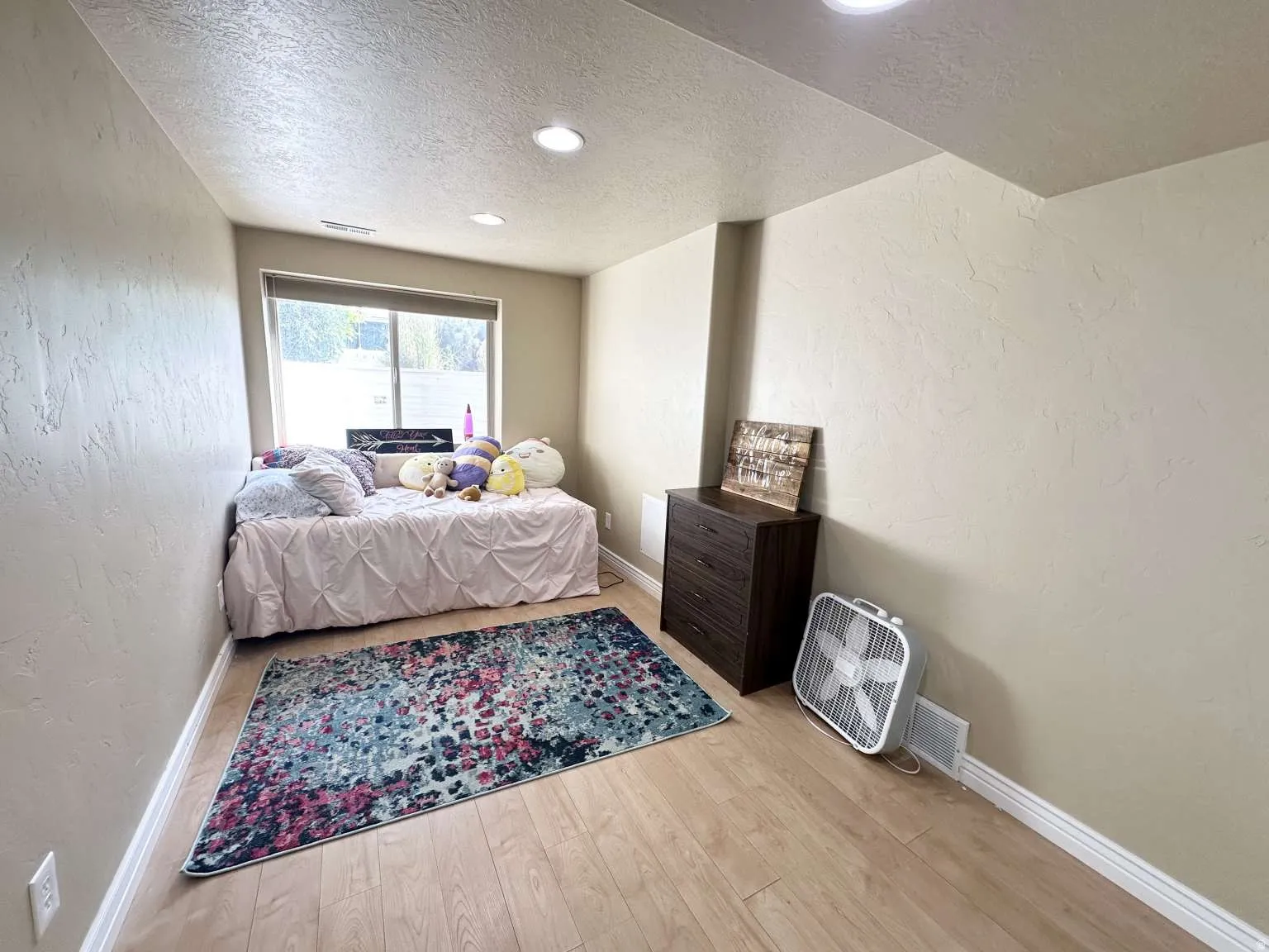 Bright room featuring a large window, light wood-finish flooring, recessed lighting, textured walls, and white baseboards
