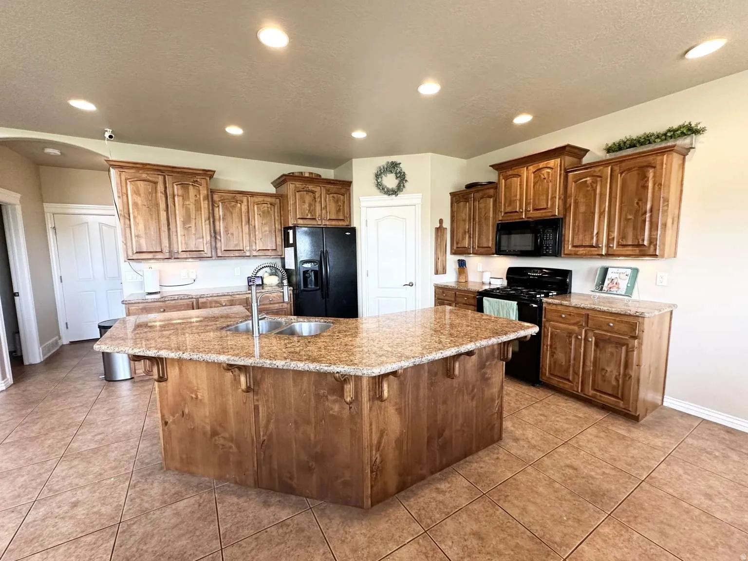 Kitchen featuring a central island with dual sinks and granite countertops, abundant wood cabinetry, black appliances including a range and refrigerator, and recessed lighting