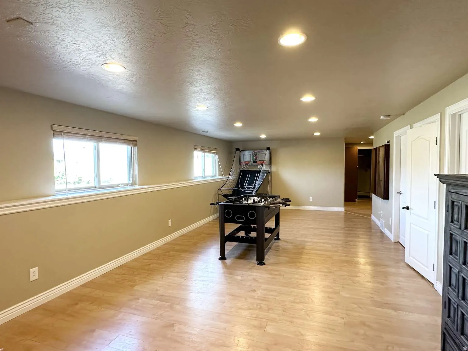 Spacious recreation room featuring light wood-finish flooring, recessed lighting, and multiple windows