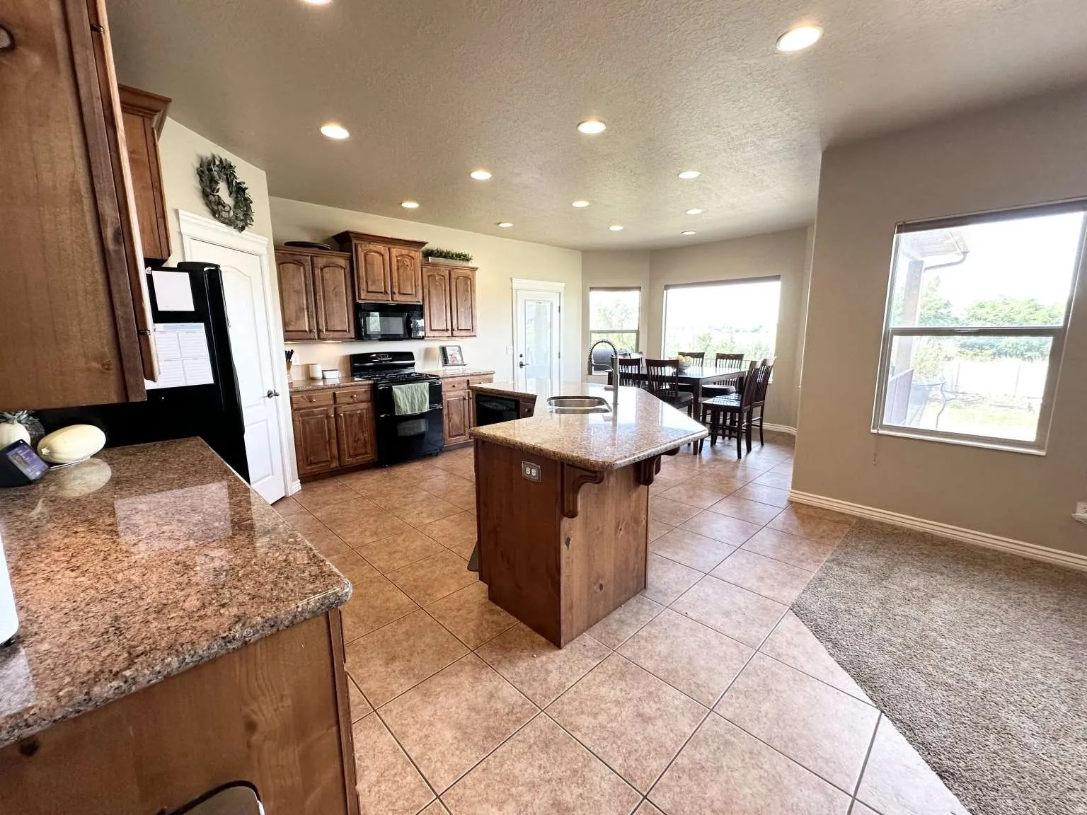 Kitchen featuring an island with a built-in sink, granite countertops, wood cabinetry, and tile flooring