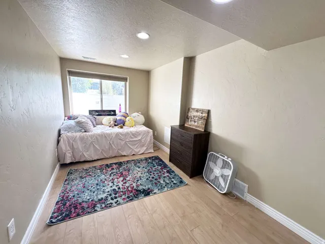 Bright room featuring a large window, light wood-finish flooring, recessed lighting, textured walls, and white baseboards