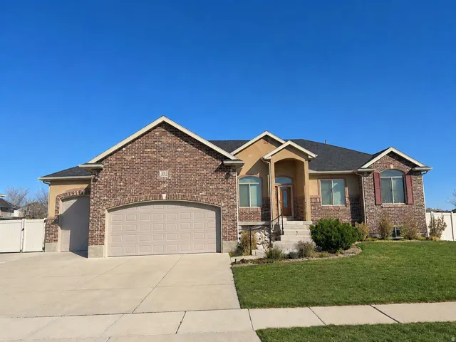 Brick and stucco exterior featuring a prominent arched entryway, a two-car garage, and established front landscaping
