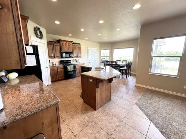 Kitchen featuring an island with a built-in sink, granite countertops, wood cabinetry, and tile flooring