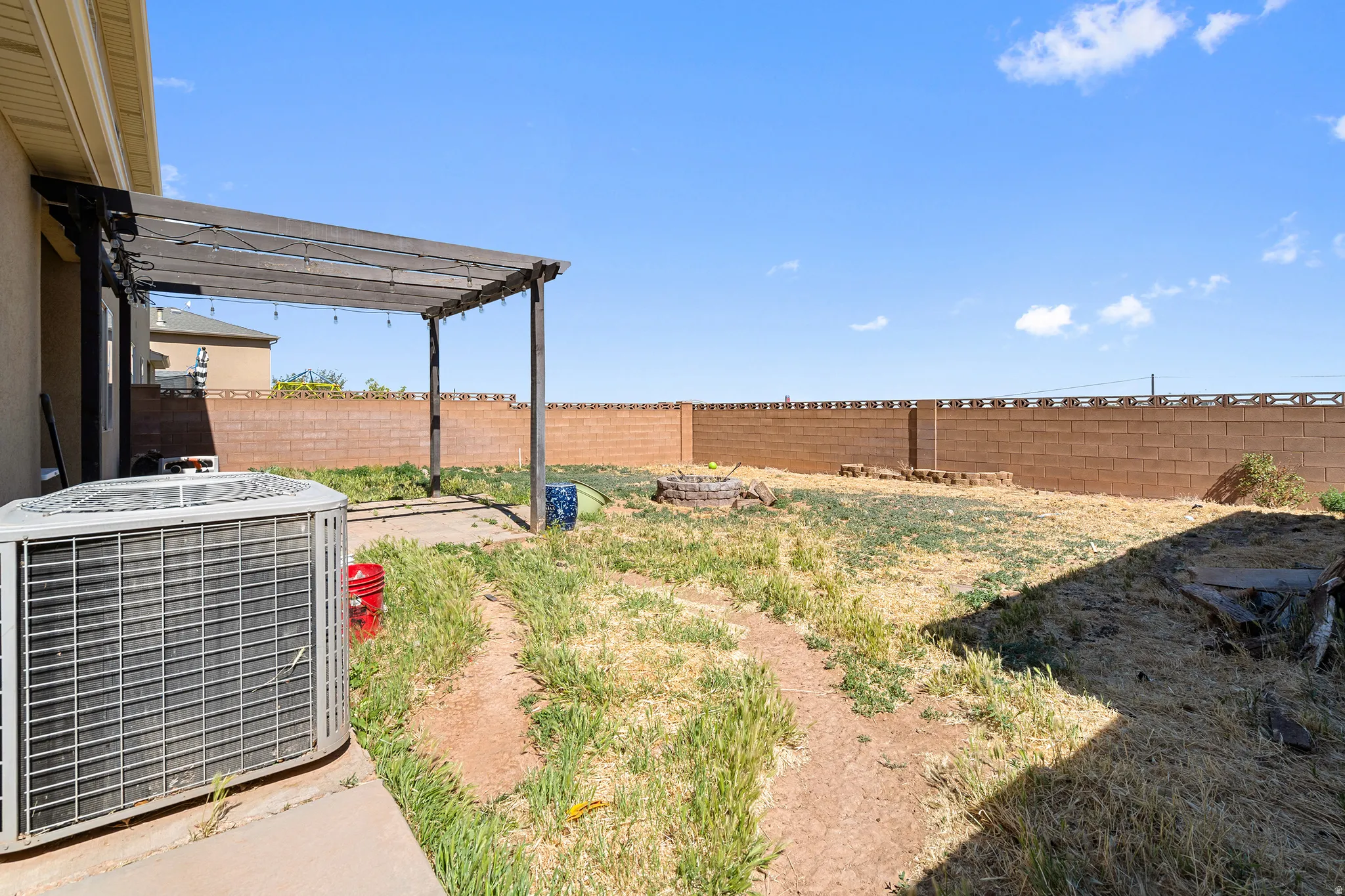 Exterior patio featuring an overhead pergola, concrete slab, and a private block wall perimeter