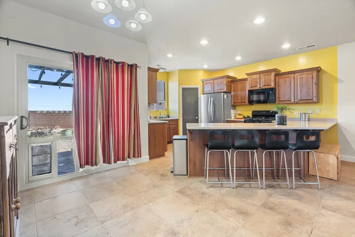 Open-concept kitchen and dining area featuring tile flooring, wood cabinetry, a breakfast bar with seating, and a glass sliding door leading to an outdoor area