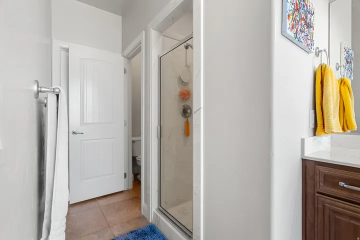 Bathroom featuring a glass-enclosed shower with marble-look wall tiling, a dark wood-finish vanity with a light countertop, a mirror, and a towel bar