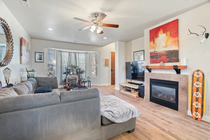 Living area featuring wood-finish flooring, a ceiling fan with integrated lighting, a bay window, and recessed lighting