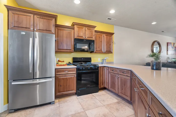 Kitchen featuring stainless steel French door refrigerator, black range with microwave above, light-toned countertops, wood cabinetry, and tiled flooring