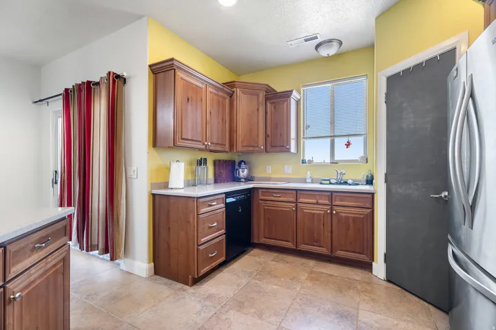 Kitchen featuring wood cabinetry, light-toned countertops, a stainless steel refrigerator, and tiled flooring