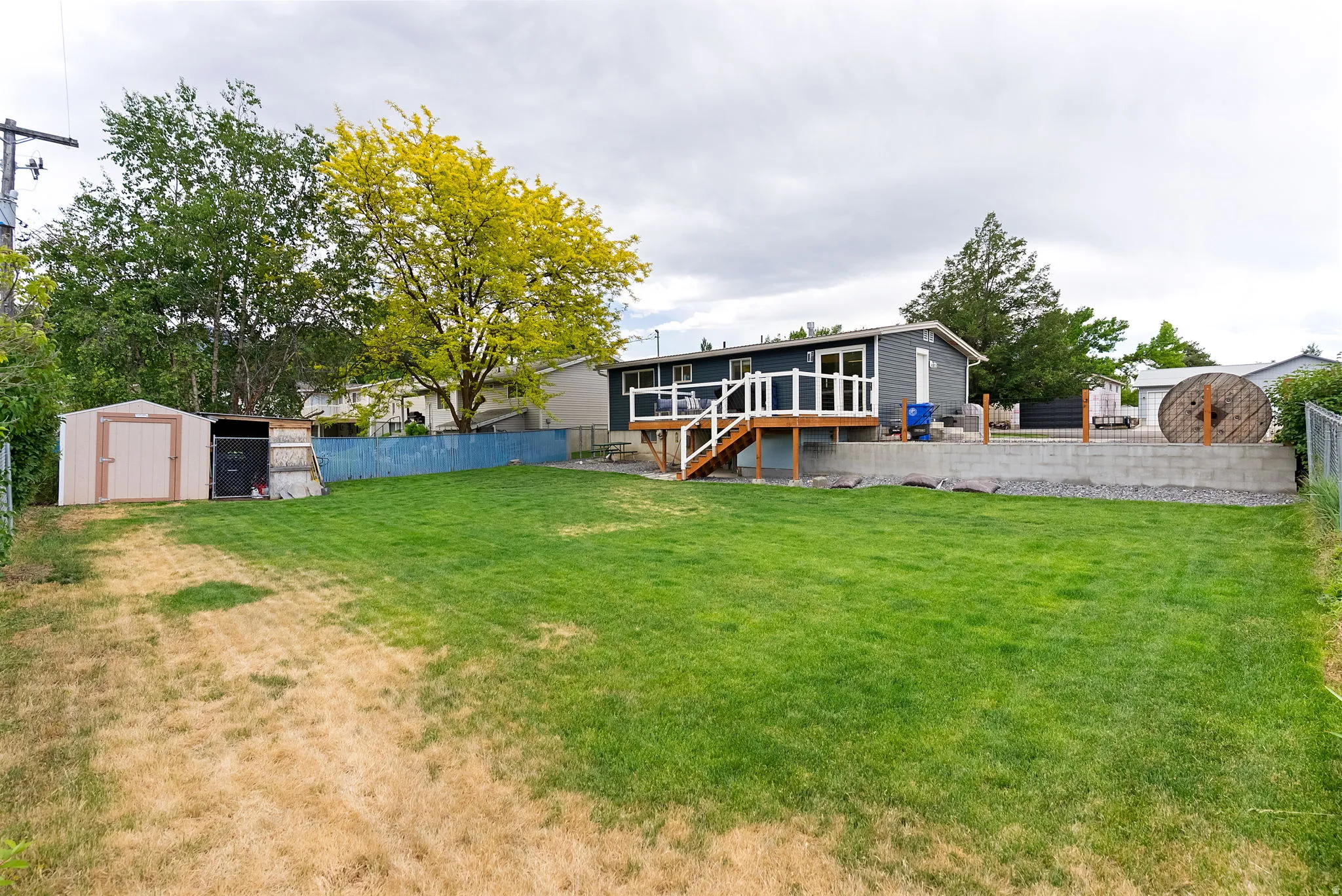 Expansive tiered backyard featuring a spacious upper-level deck, a concrete retaining wall, and two storage sheds