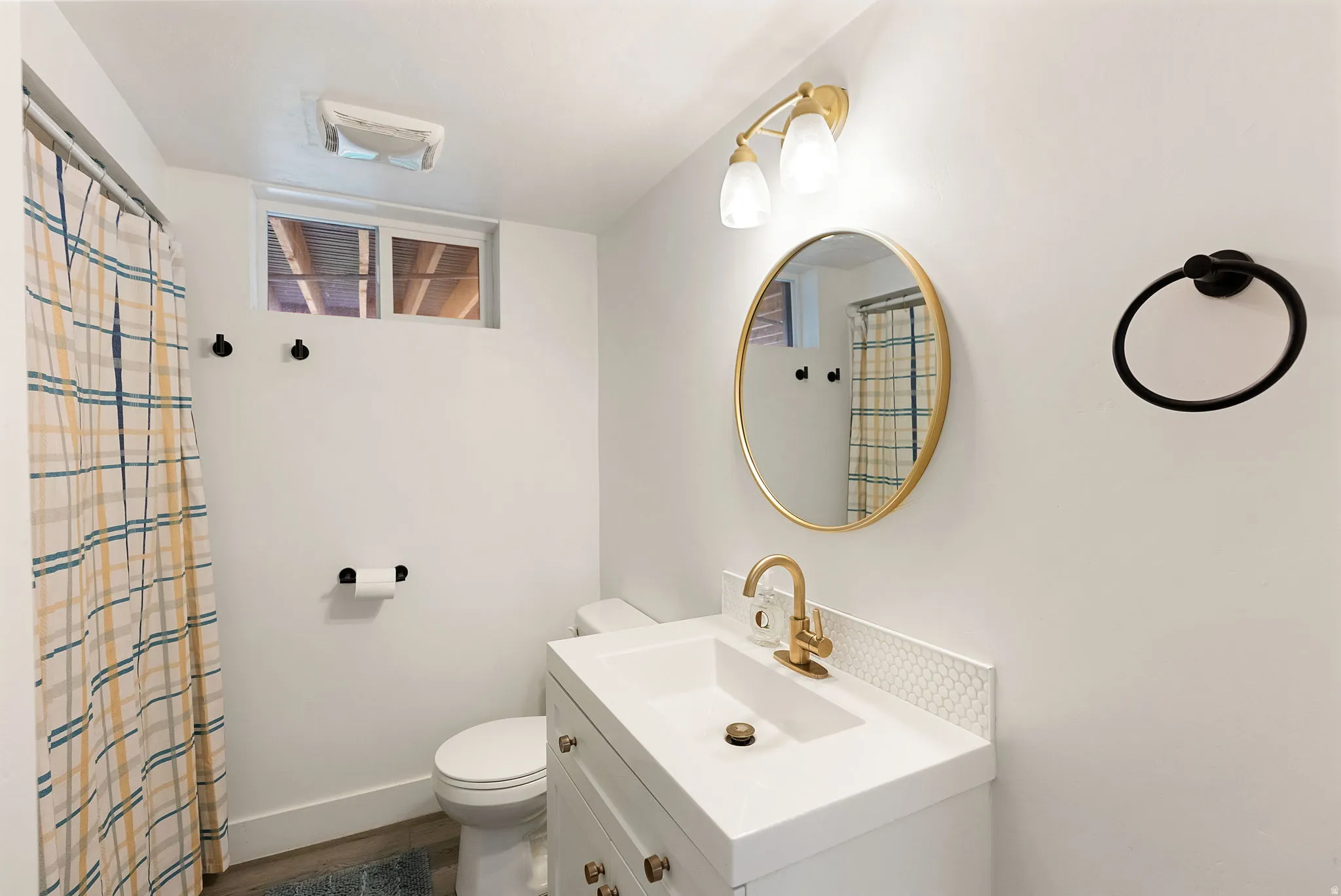 Bathroom featuring a white vanity with integrated sink, brass-finish faucet, and a circular gold-framed mirror