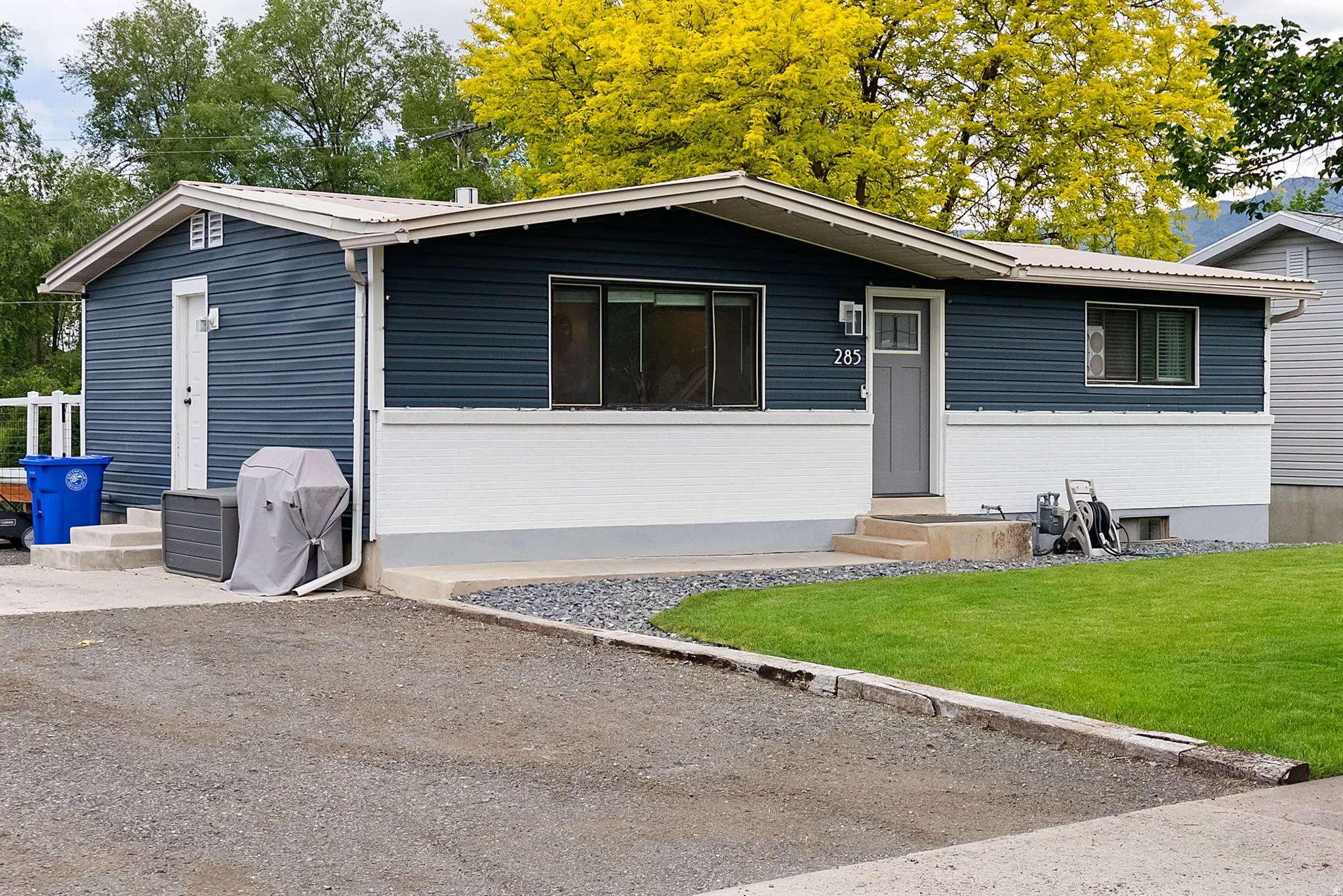 Single-story exterior featuring dark blue siding, white foundation, and a gray front door with a transom window