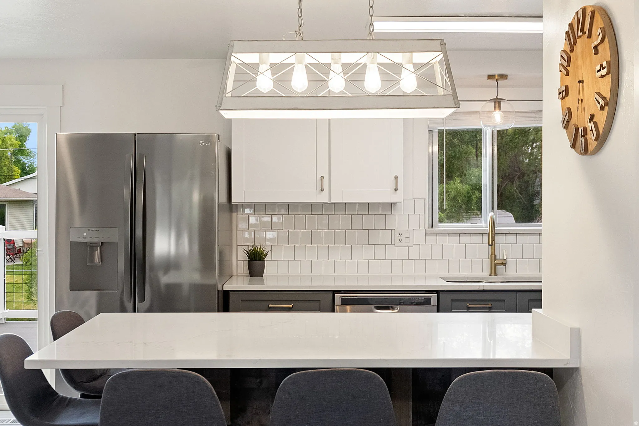 Modern kitchen featuring a white quartz countertop island, stainless steel side-by-side refrigerator, white subway tile backsplash, white upper cabinetry, and contrasting dark lower cabinetry