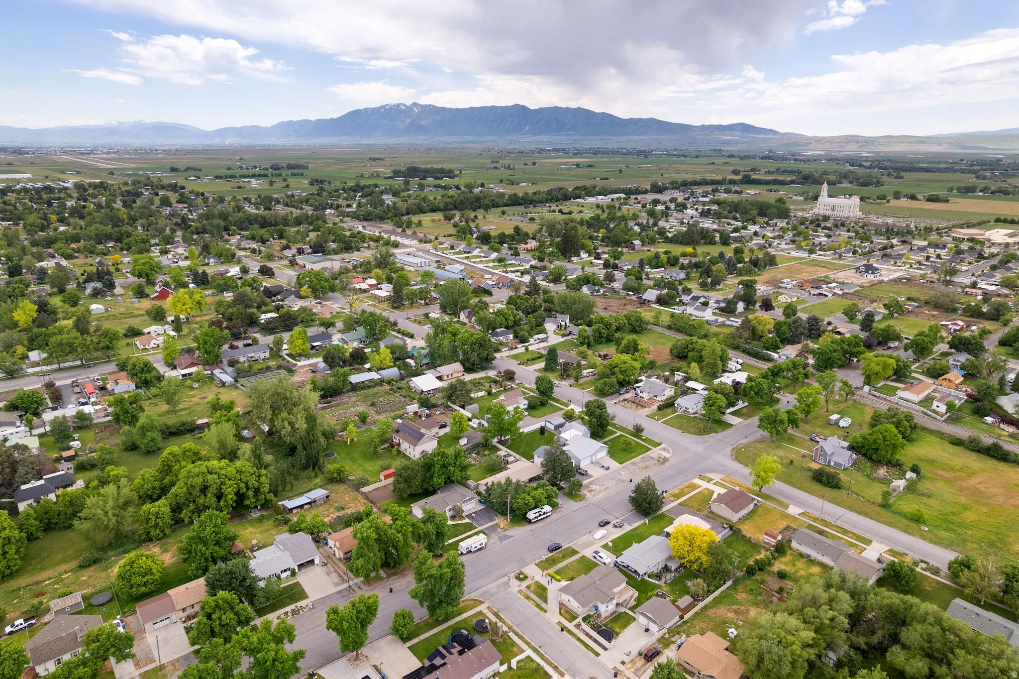 Expansive aerial landscape featuring a residential neighborhood with mature trees, green fields, and distant mountains