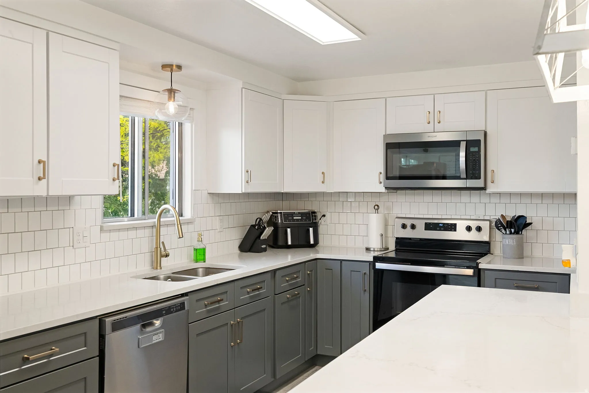 Kitchen featuring two-tone cabinetry with gold-tone hardware, white subway tile backsplash, and light-toned countertops