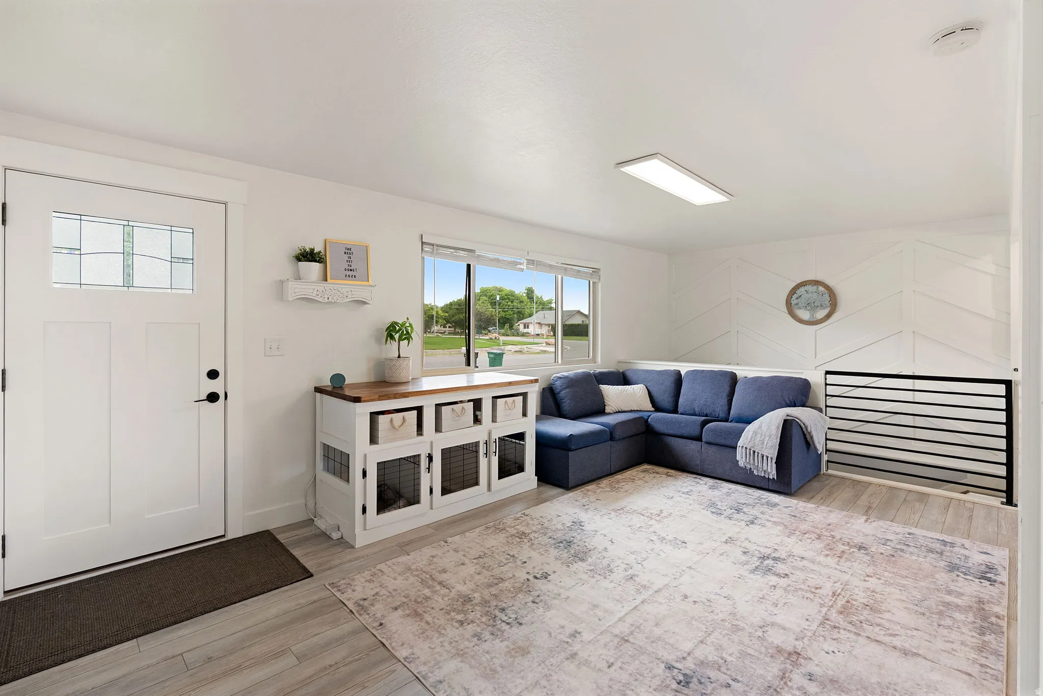 Light-filled living space with wood-finish flooring, a contemporary accent wall, and a horizontal metal railing