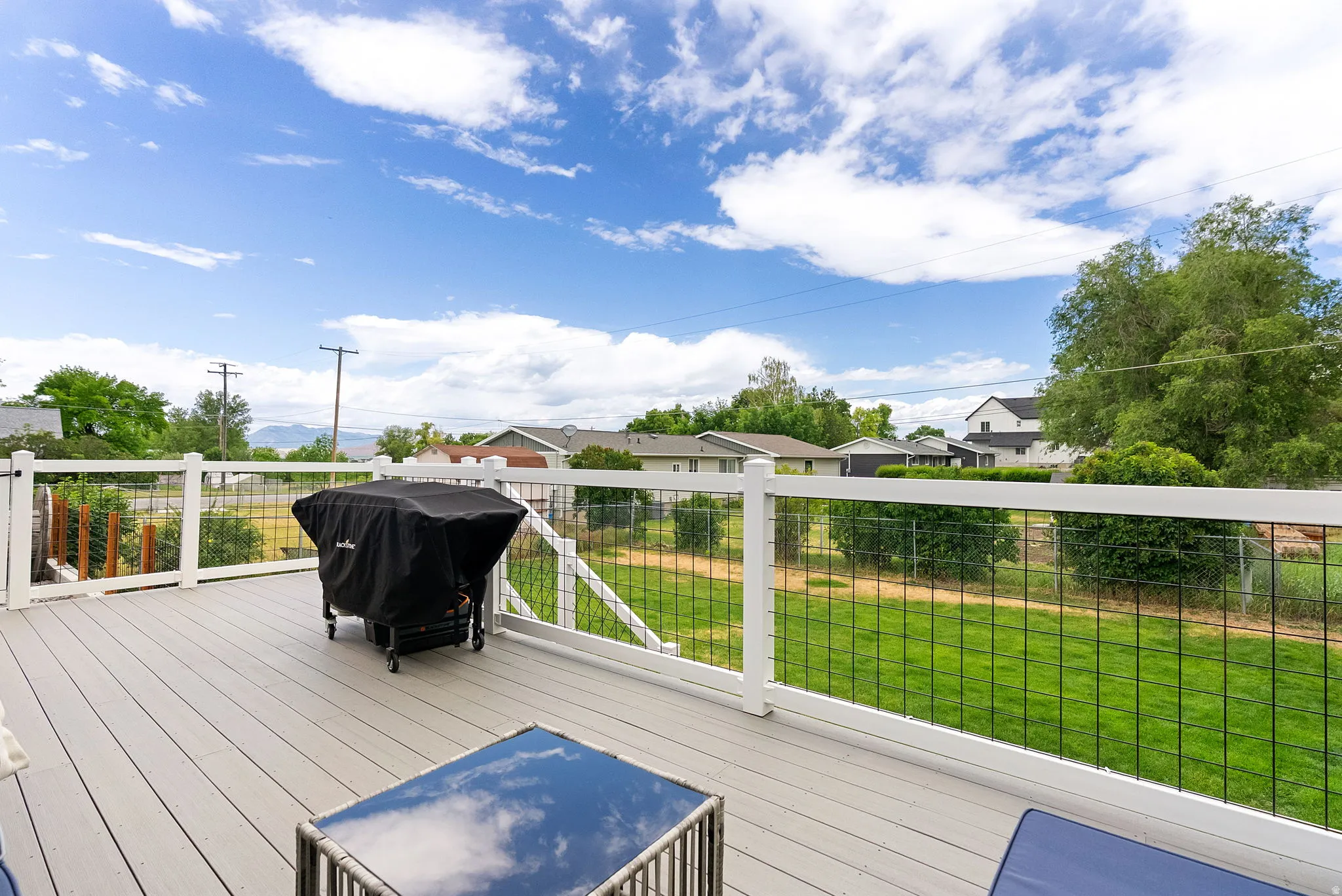 Spacious outdoor deck featuring composite decking, white railing with black mesh infill, and a lush green lawn beyond