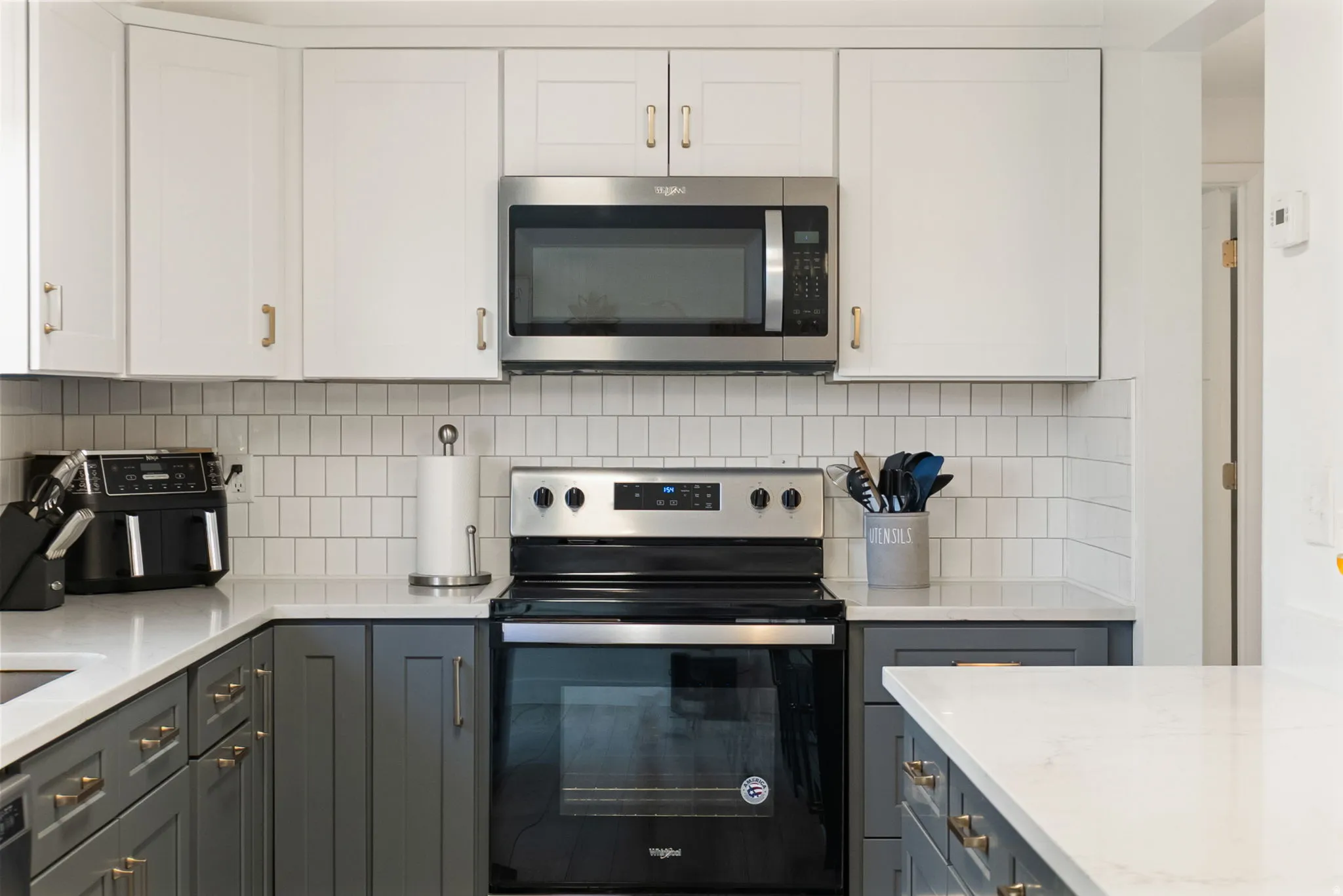 Kitchen featuring stainless steel appliances, a white subway tile backsplash, white upper cabinetry, and gray lower cabinetry with gold-toned hardware